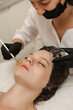 The cosmetologist applies a liquid gel to the face with a wide brush, the carboxytherapy procedure and its preparations.