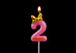 Burning pink birthday candle with golden bow isolated on black background, number 2.	