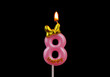 Burning pink birthday candle with golden bow isolated on black background, number 8.	