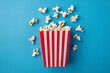 Fluffy popcorn in red strip paper bucket on blue background. Copy space for text. Cinema and movie theater concept	