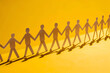 A row of paper people holding hands on yellow background