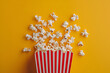 Fluffy popcorn in red strip paper bucket on yellow background. Copy space for text. Cinema and movie theater concept	