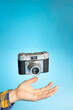 Hand with a vintage camera suspended in the air on a light blue background. Photography day concept