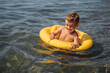Cute baby boy swims in a yellow inflatable circle in the sea on the beach.