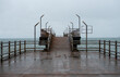 Empty pier extends into sea under grey sky, reflecting serene and moody atmosphere on rainy day.