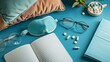 Topview image showcasing a sleep mask, notebooks, eyeglasses, and pills on a blue surface