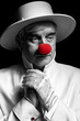 Close-up selective color portrait of sad clown. An elderly man in a white coat and hat.
