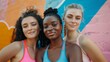 © Iona - Three young women of diverse ethnic backgrounds pose together in front of a colorful mural, showcasing vibrant fitness attire