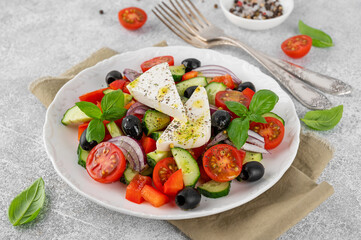 Wall Mural - Greek salad of fresh juicy vegetables, feta cheese, herbs and olives on a white plate on a light concrete background. Healthy food. Copy space, top view.