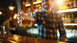 © BOONJUNG - Young man holding glass of whiskey at bar counter with bartender in background in nightclub