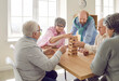 Group of senior men and women playing together with wooden building blocks for dementia therapy in nursing home enjoying activity sitting at the table. Leisure in retirement home concept.