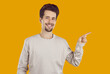 Cheerful young man pointing his finger to empty space. Portrait of handsome bearded man wearing casual clothes gesturing on yellow background pointing to side at copy space