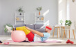 Funny young man in sportswear having home workout lying on floor on yoga mat with fit ball. Sporty male person exercising at home. Sport, fitness, health and home training concept.