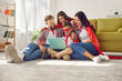 Happy mum, dad and kids dressed in red capes relaxing on holiday weekend, sitting on floor rug with laptop PC device, watching family film about strong hero with super power, having good time together