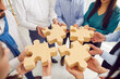 Top view hands of a group of business people assembling big wooden puzzle. Coworkers join jigsaw pieces in office finding solution, working on project together. Support in teamwork concept.