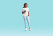Portrait of young happy smiling african american woman employee or student girl in white t-shirt and jeans holding clipboard with paper documents in hand isolated on studio blue background.