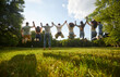Group of friends jumping in air with raised hands while having fun in summer park. Rear view of people standing in row, holding hands and jumping up together against background of blue sky. Back view.