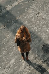 Wall Mural - A woman wearing a brown coat stands on a sidewalk