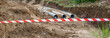 New fiber glass water pipeline in trench. Replacement of old rusty tubes by new one, surrounding with Red white warning tape barrier ribbon swinging in the wind
