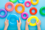 Fototapeta Tulipany - Little children hands holding colorful plastic rings on light blue table background. Pastel color. Toys of development for kids. Playing together. Point of view shot. Closeup. Top down view.