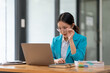© amnaj - Asian businesswoman holding glasses and looking intently at her laptop computer in the office.