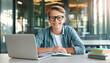 © Janire Fernández - Empowered Scholar: Portrait of a Confident Student Boy Grinning for the Camera, Seated at His Desk with Laptop and Textbook, Demonstrating His Dedication and Passion for Learning