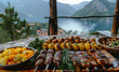 Grilled meat and vegetables on wooden table against the background of the lake and mountains