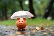 A piggy bunk is standing with umbrella under the rain, a pile of coins on the ground, concept of financial safety in hard economic conditions