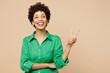 © ViDi Studio - Young smiling happy fun woman of African American ethnicity wear green shirt casual clothes showing victory sign look camera isolated on plain pastel light beige background studio. Lifestyle concept.