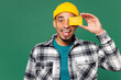 Young man of African American ethnicity wear shirt blue t-shirt yellow hat hold in hand cover eye with mock up of credit bank card isolated on plain green background studio portrait Lifestyle concept