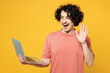 Young shocked surprised happy IT man he wear pink t-shirt casual clothes hold use work on laptop pc computer waving hand isolated on plain yellow orange background studio portrait. Lifestyle concept.