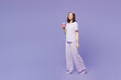 Full body young calm woman wear pyjamas jam sleep eye mask rest relax at home hold takeaway delivery craft paper cup coffee to go walk isolated on plain purple background. Good mood night nap concept.