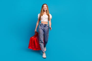 Sticker - Full size photo of nice young girl walk hold bags empty space wear top isolated on blue color background