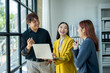 © Wasana - Three people are standing in a room, smiling and talking to each other. One of them is holding a laptop