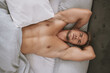 Muscular man and stretching arms behind head in bed for rest, relax and fatigue at home on weekend. Male person or model with above on pillow and blanket for comfort, stress relief and portrait