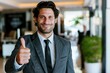 © id512 - confident smiling businessman showing thumb up gesture in a modern office, success positive outlook concept
