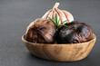 Bulbs of black garlic and rosemary in a wooden bowl on a gray background.