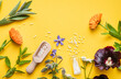 Above view of homeopathic medicine pills in jars and spilled around on yellow background, decorated with fresh various herbs and plants. Homeopathy border background, lot of copy space.