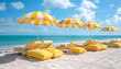 Beach with yellow and white striped lounge chairs, yellow and white striped umbrellas, with solid yellow pillows on lounge chairs