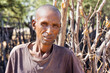 African village, adult man with wrinkles in front of the outdoors kitchen, in the yard