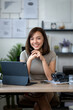 © Wasana - A woman is sitting at a desk with a laptop and a tablet. She is smiling and she is happy