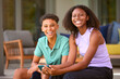 © Monkey Business - Portrait Of Teenage Brother And Sister With Mobile Phone Sitting Outdoors At Home On Deck