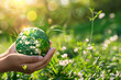 Hands holding a green earth globe against a sunny background