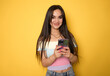 © Danko - Portrait of a smiling casual woman holding smartphone over yellow background