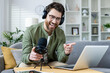Cheerful male podcaster in headphones recording a live podcast. He is gesturing and smiling warmly at his comfortable home setup.