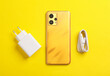 New smartphone with cable and charging adapter on yellow background
