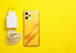 New smartphone with cable and charging adapter on yellow background