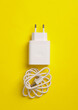 White charger adapter with cable for charging phone on yellow background