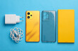 New yellow smartphone with box and accessories on blue background. Modern gadgets, unboxing. Flat lay. Top view