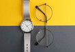 Stylish wristwatch with eyeglasses on yelow gray background. Women's accessories. Top view